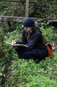 art journaling and nature journaling with Alex Boon. In this photo you can see Alex crouching down in the field and working in his sketchbook.