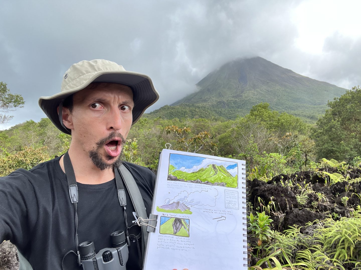marley peifer nature journaling in costa rica at the arenal volcano showing his nature journal with watercolor sketches of the volcano in the background